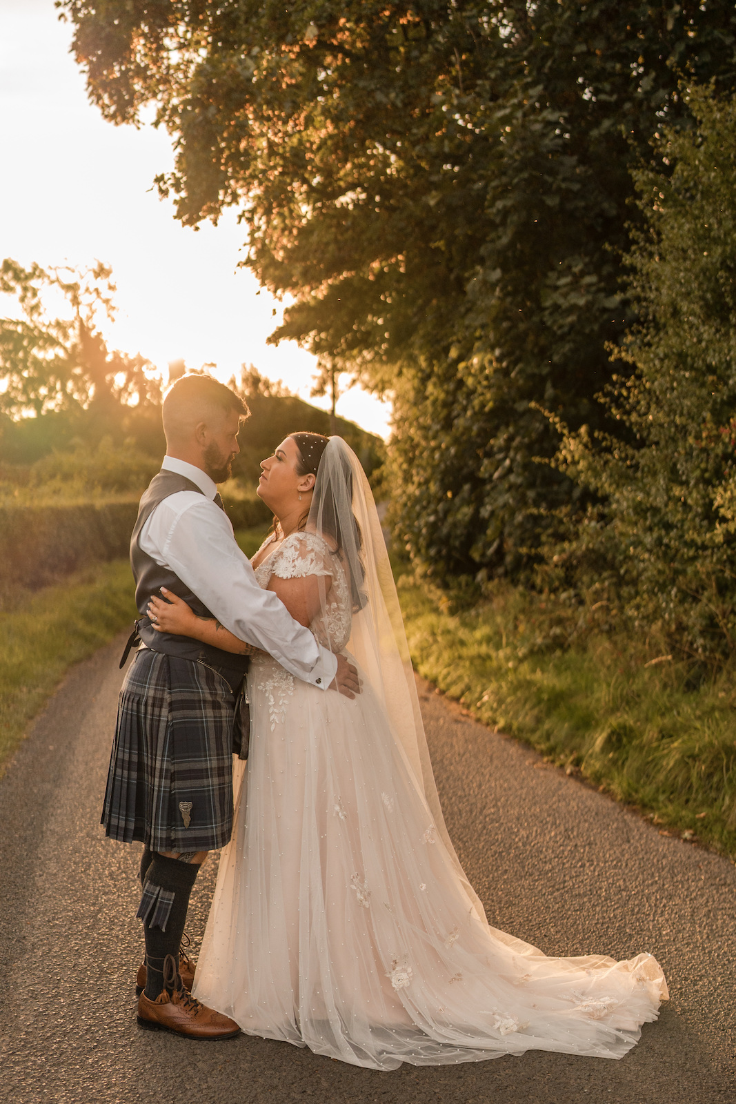 Ashley & Derek Bride and groom facing each other on a country road with the sun behind them