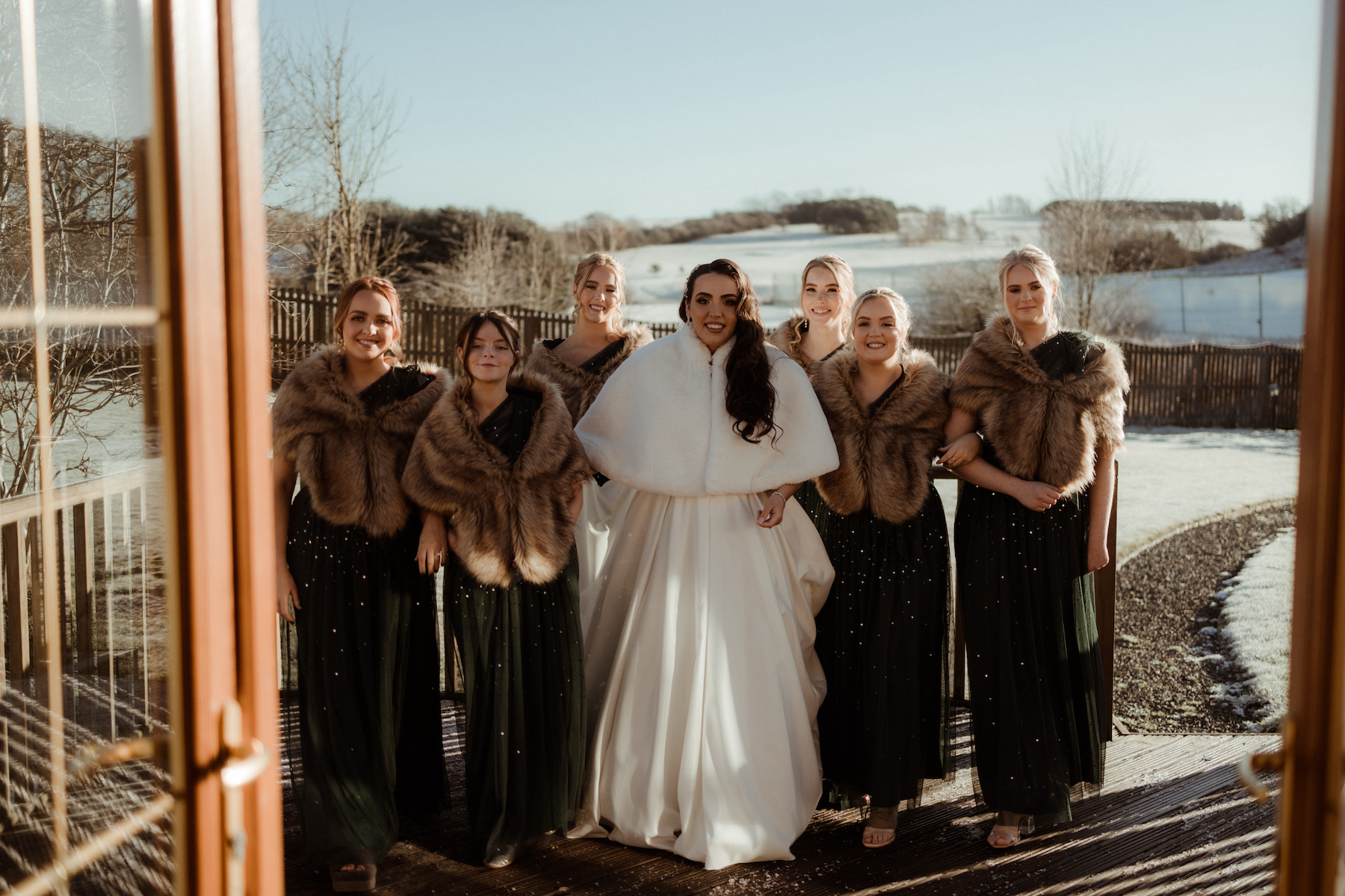 Bride and bridesmaids dressed in fur wraps standing outside in the winter sunshine at Roodlea Barn.
