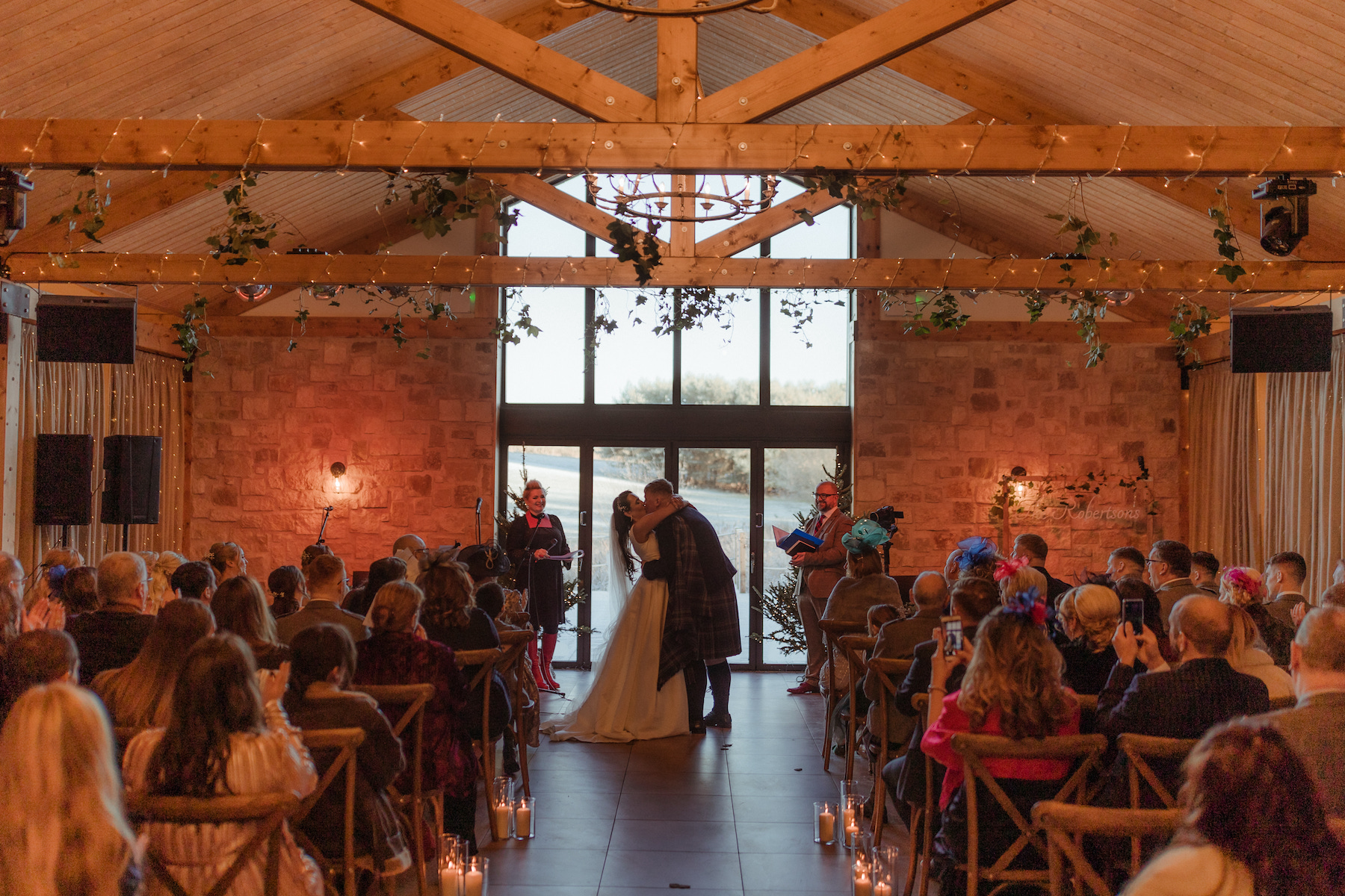 Bride and groom sharing their first kiss during a winter wedding ceremony inside Roodlea Barn.