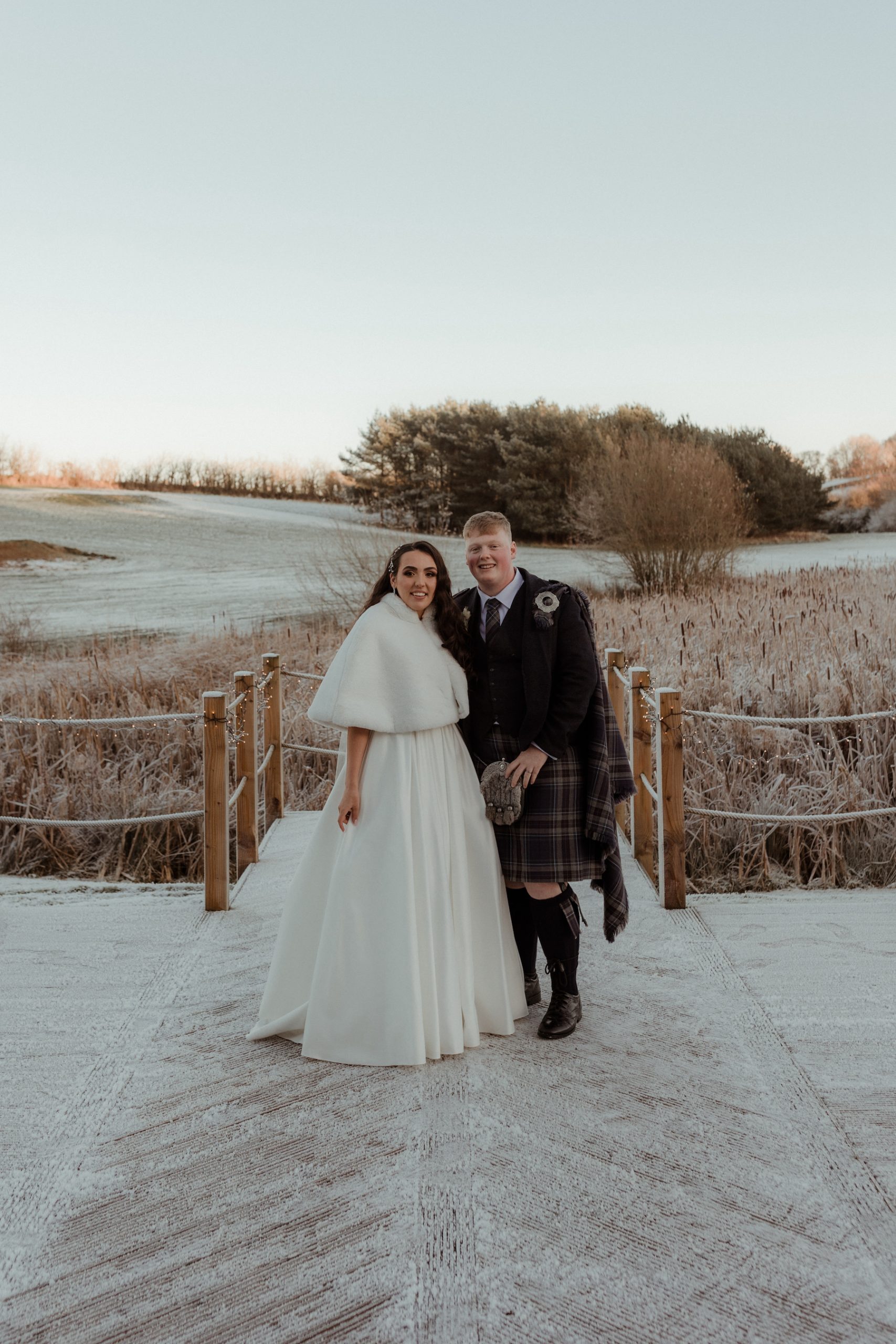 Bride and groom standing on a frosty decking surrounded by winter scenery at Roodlea Barn.