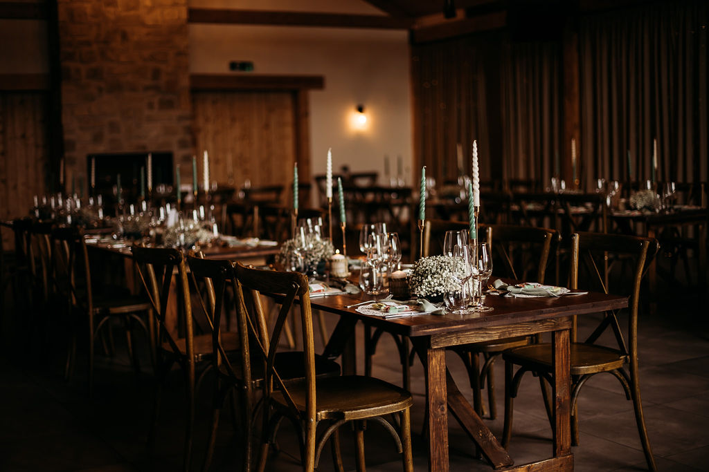Rustic wedding reception tables set with taper candles, glassware and gypsophila centrepieces inside Roodlea Barn.