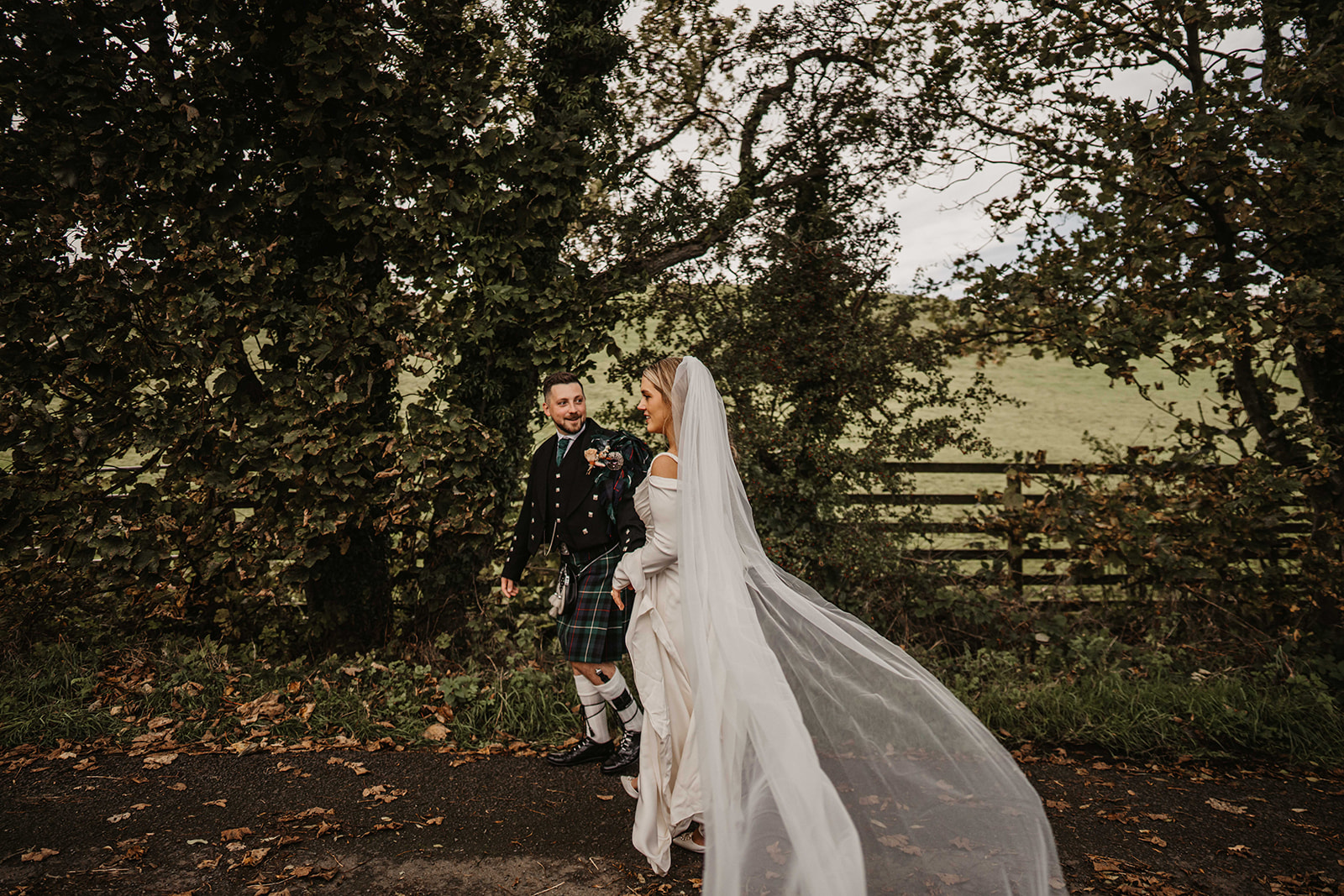 Bride and groom sharing an intimate moment on a quiet countryside road surrounded by autumn foliage.