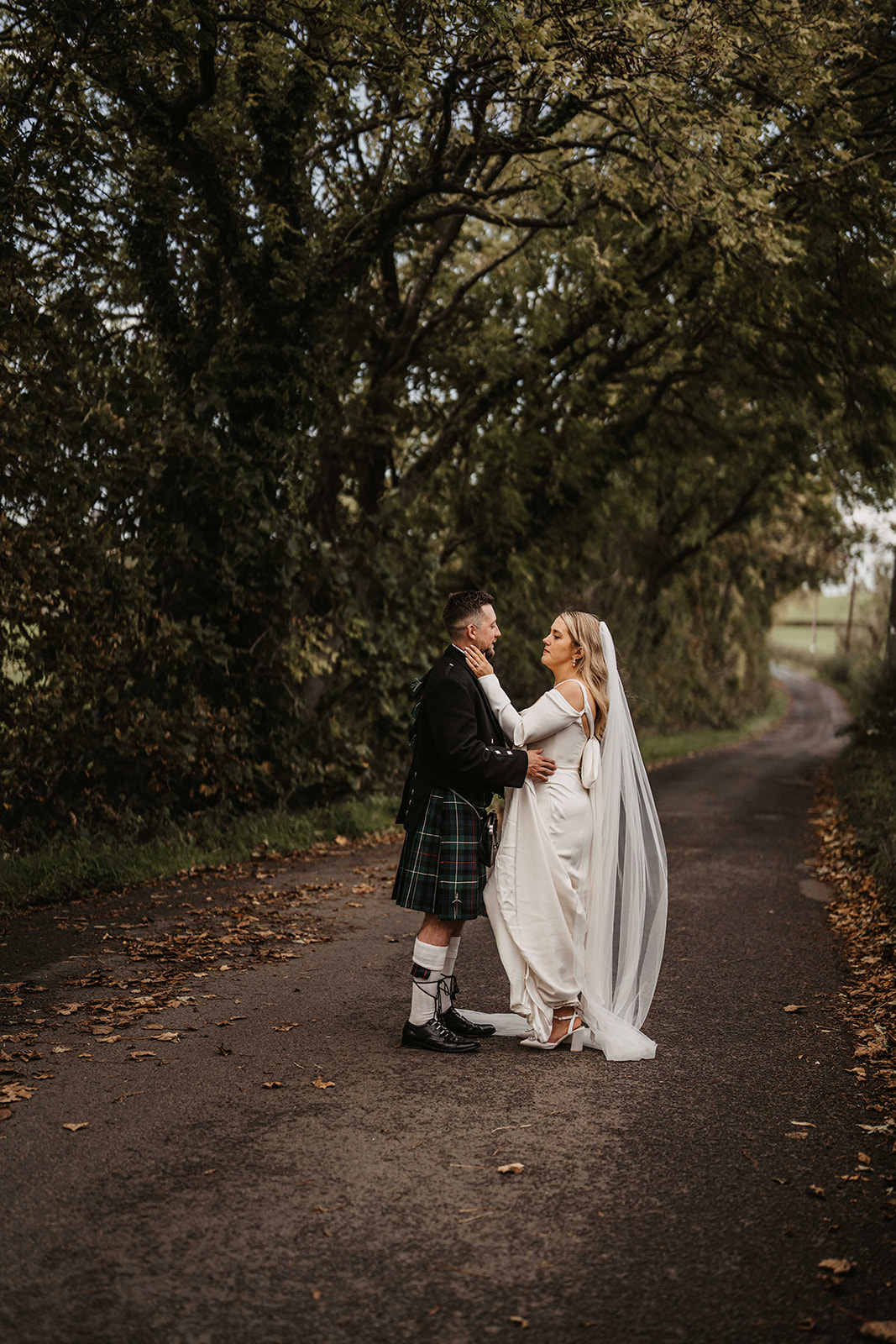 ride and groom walking together along a tree lined country lane on their wedding day at Roodlea Barn.