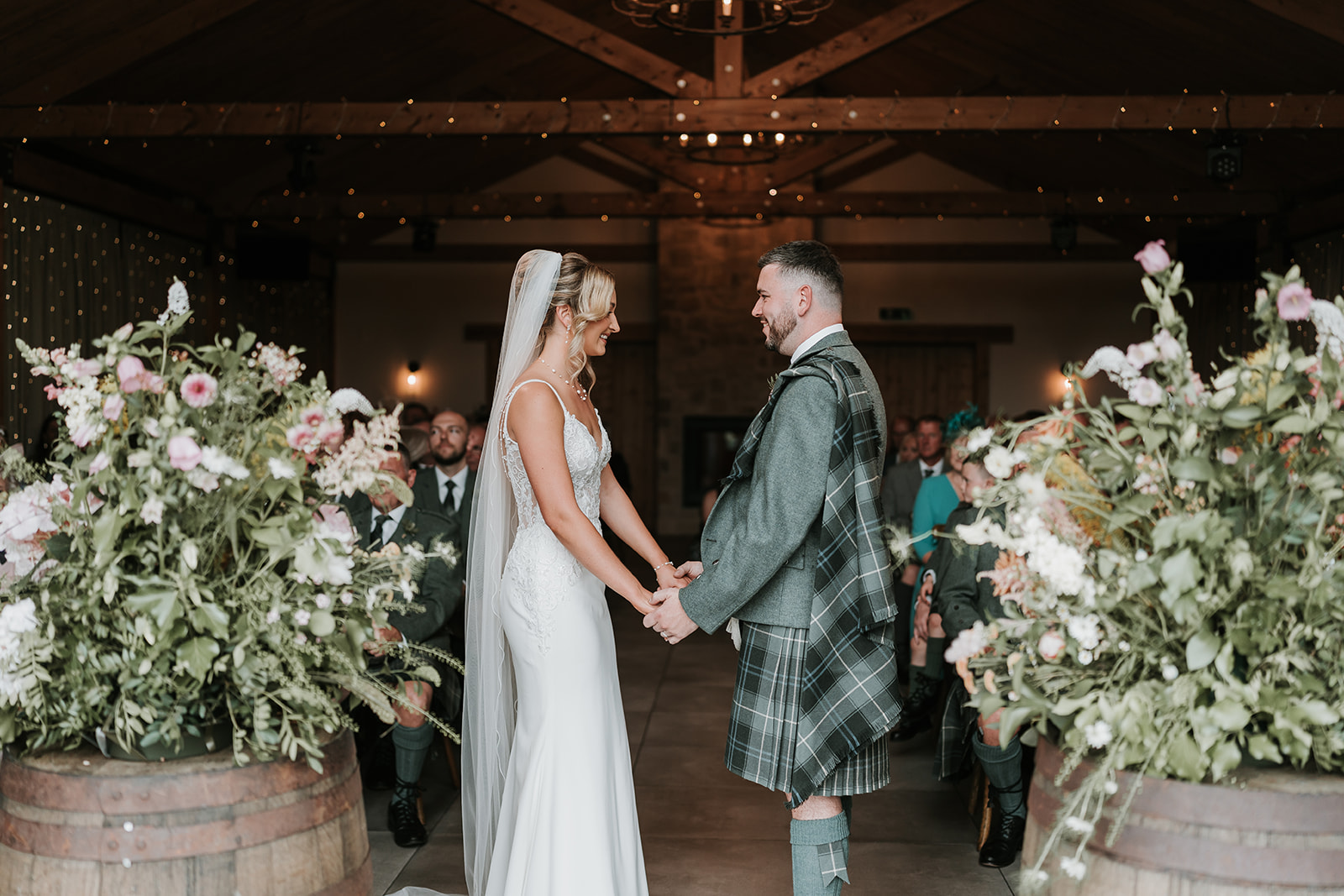 Bride & groom getting married in barn venue with wooden beams and fairy lights